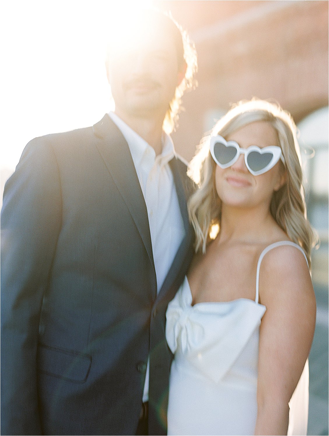 Golden hour engagement session in Fells Point with film wedding photographer, Renee Hollingshead. Bride is wearing white heart sunglasses