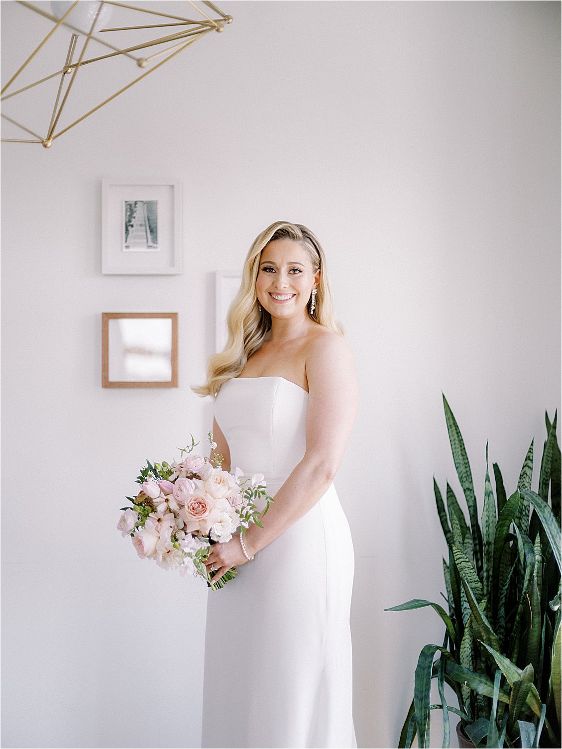 Bride in a modern strapless chic wedding gown with soft hollywood waves and a pink bouquet