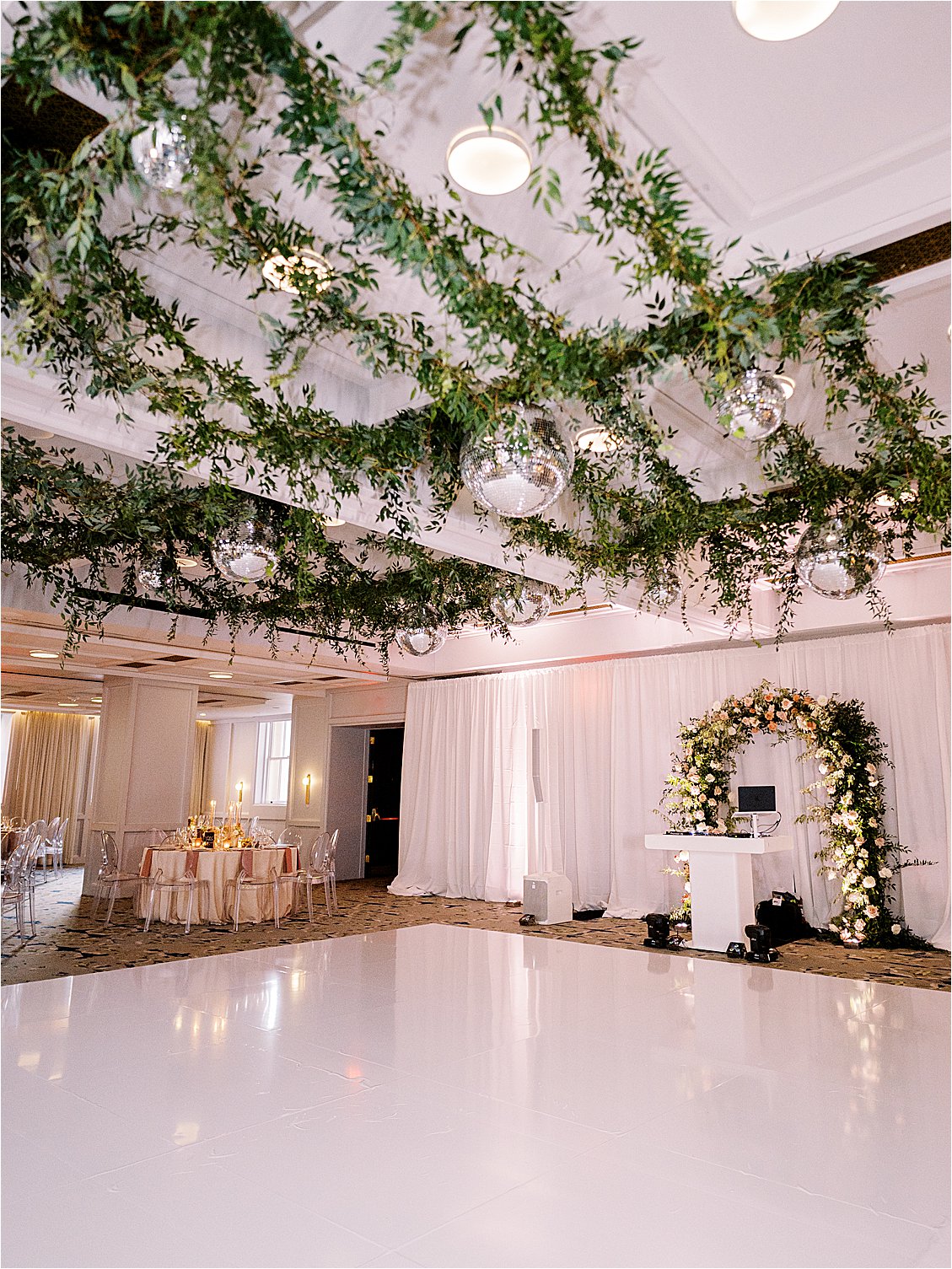Garden Disco wedding reception with greenery installation filled with disco balls, white wrapped dance floor and repurposed ceremony arch