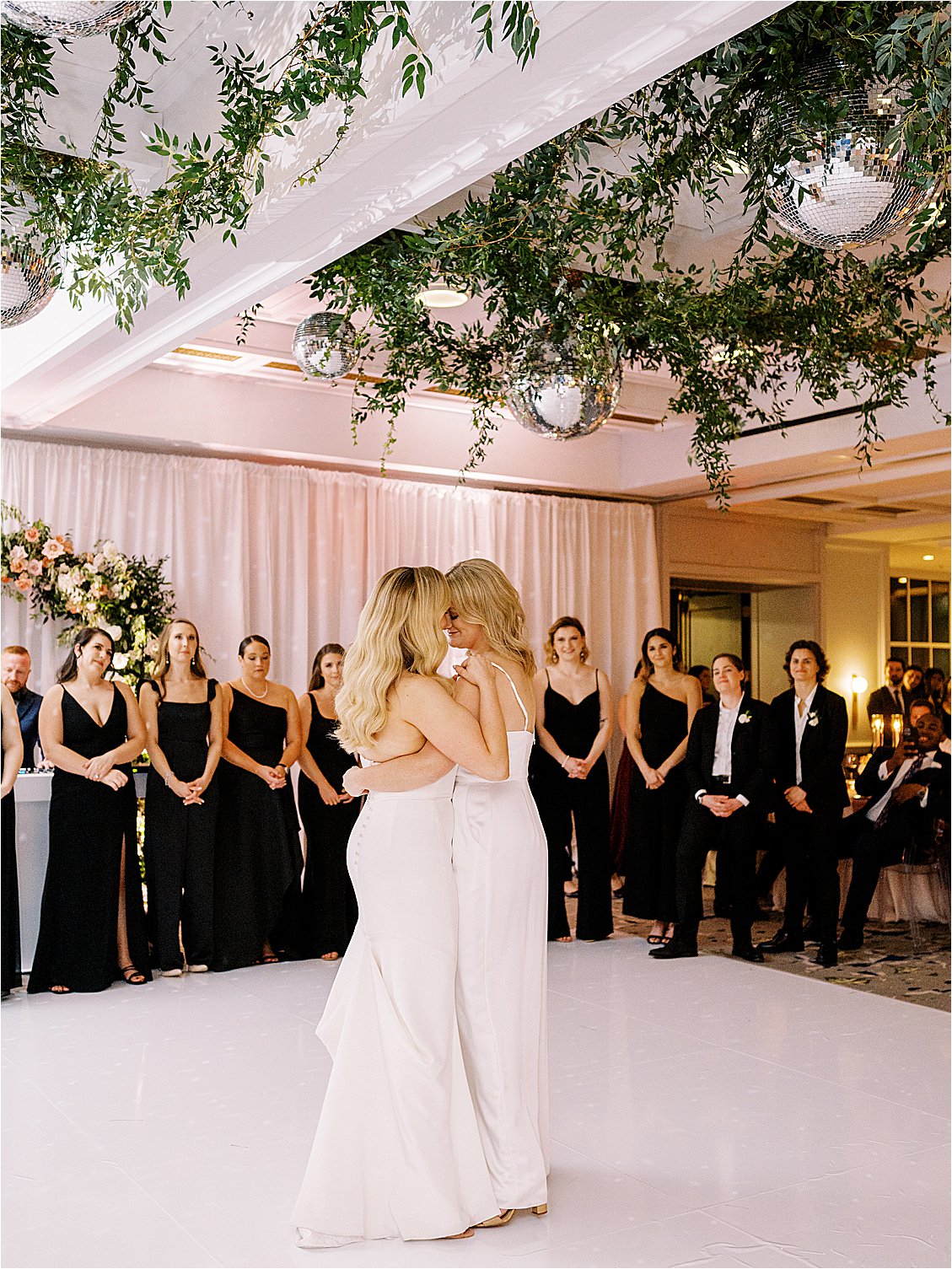 Brides share their first dance under a ceiling installation of greenery and disco balls