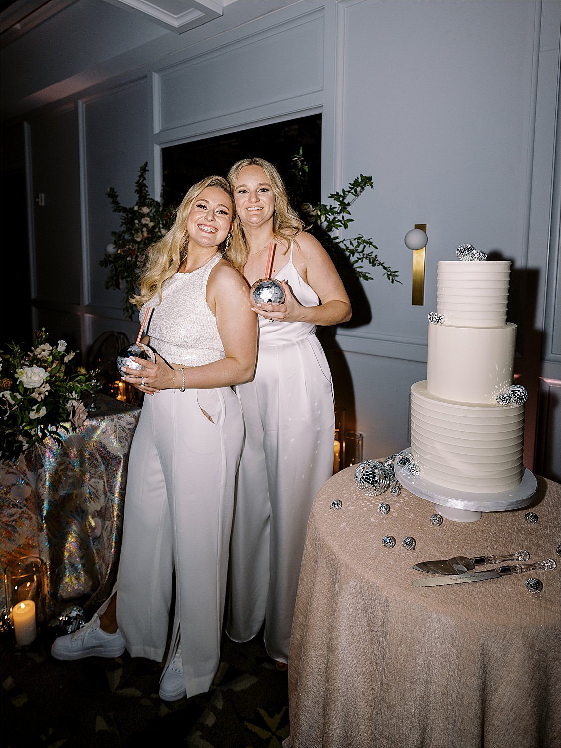 Brides holding a disco ball cup and cutting their disco ball three-tiered wedding cake