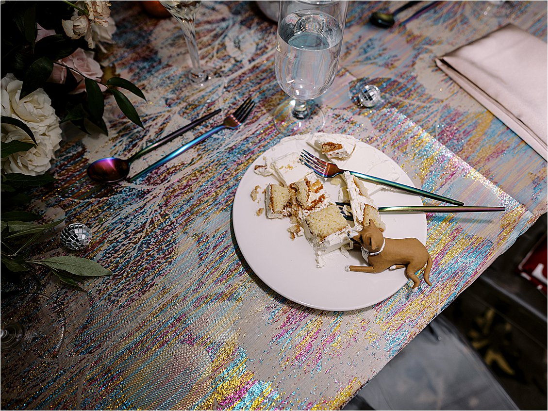 Cut wedding cake and their fondant dog replica on an iridescent rainbow linen