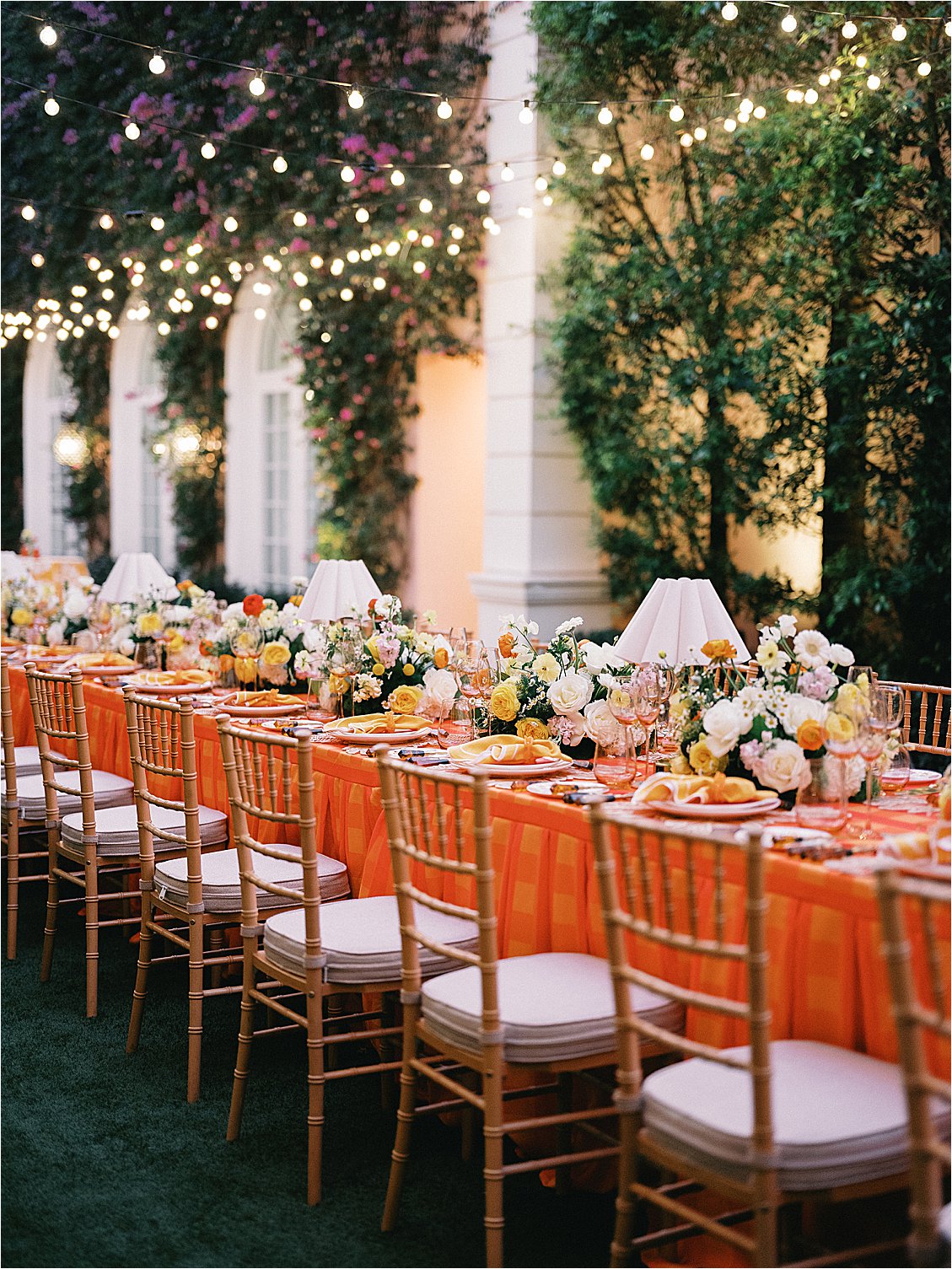 Full-length view of the corporate dinner table dressed in bold orange plaid under a canopy of café string lights in The Colony Hotel East Garden, Palm Beach, designed by Gramercy & Grace for Zoe Strollers retreat