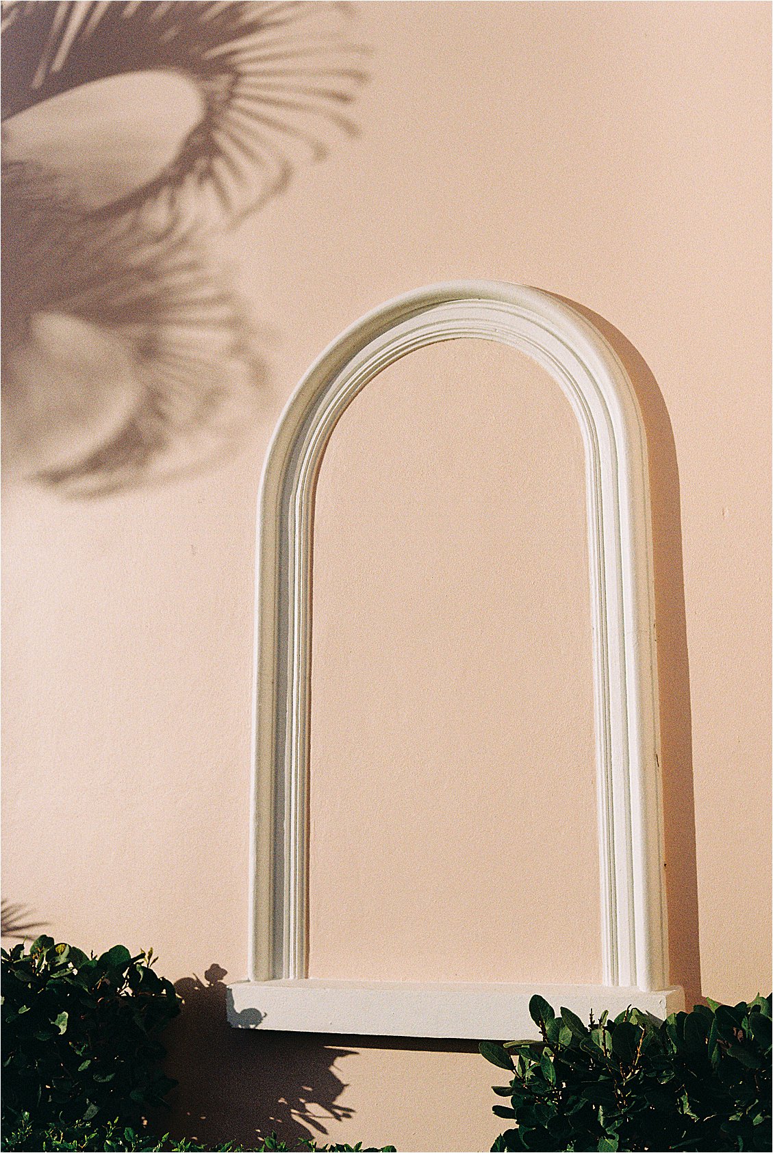 White molded arch architectural detail against the blush pink exterior wall of The Colony Hotel Palm Beach with tropical palm shadow, corporate event photography by Renee Hollingshead 