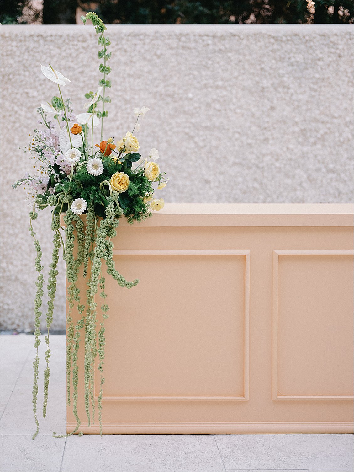 Cascading floral arrangement with yellow garden roses, white gerbera daisies, anthurium, and trailing amaranthus greenery on a peach paneled bar at The Colony Hotel Palm Beach corporate event by Gramercy & Grace
