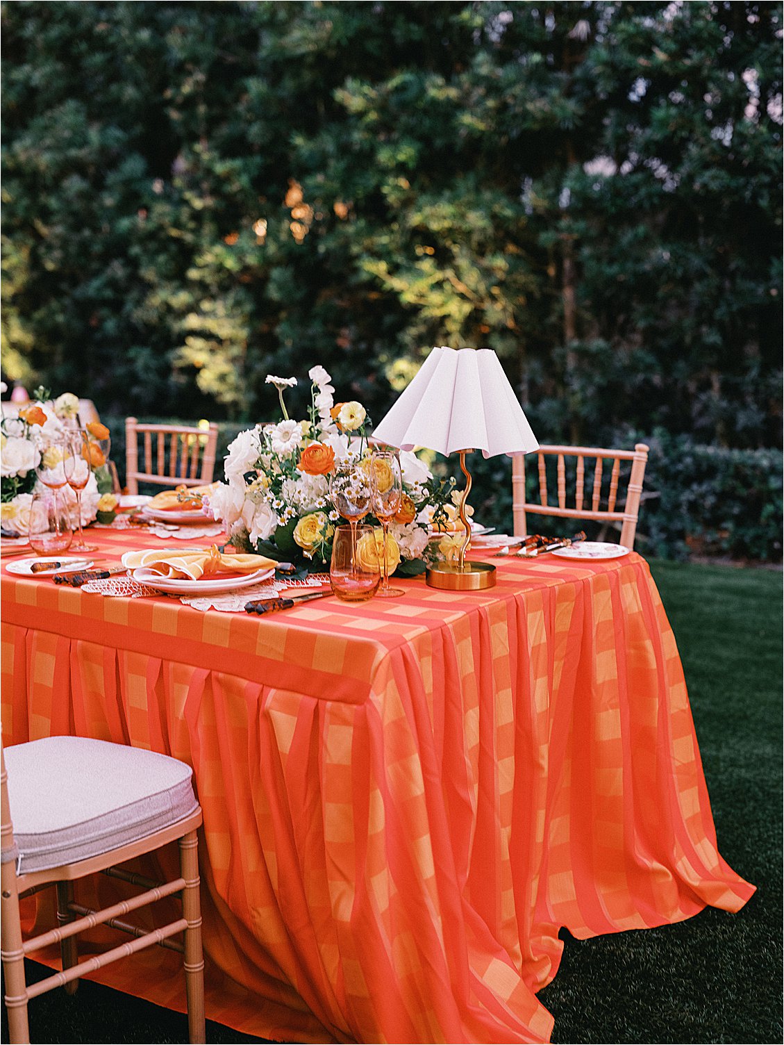 Wide shot of the corporate dinner table set with bold orange plaid tablecloth, gold chiavari chairs, white table lamps, and citrus floral centerpieces in The Colony Hotel East Garden, styled by Gramercy & Grace for Zoe Strollers 
