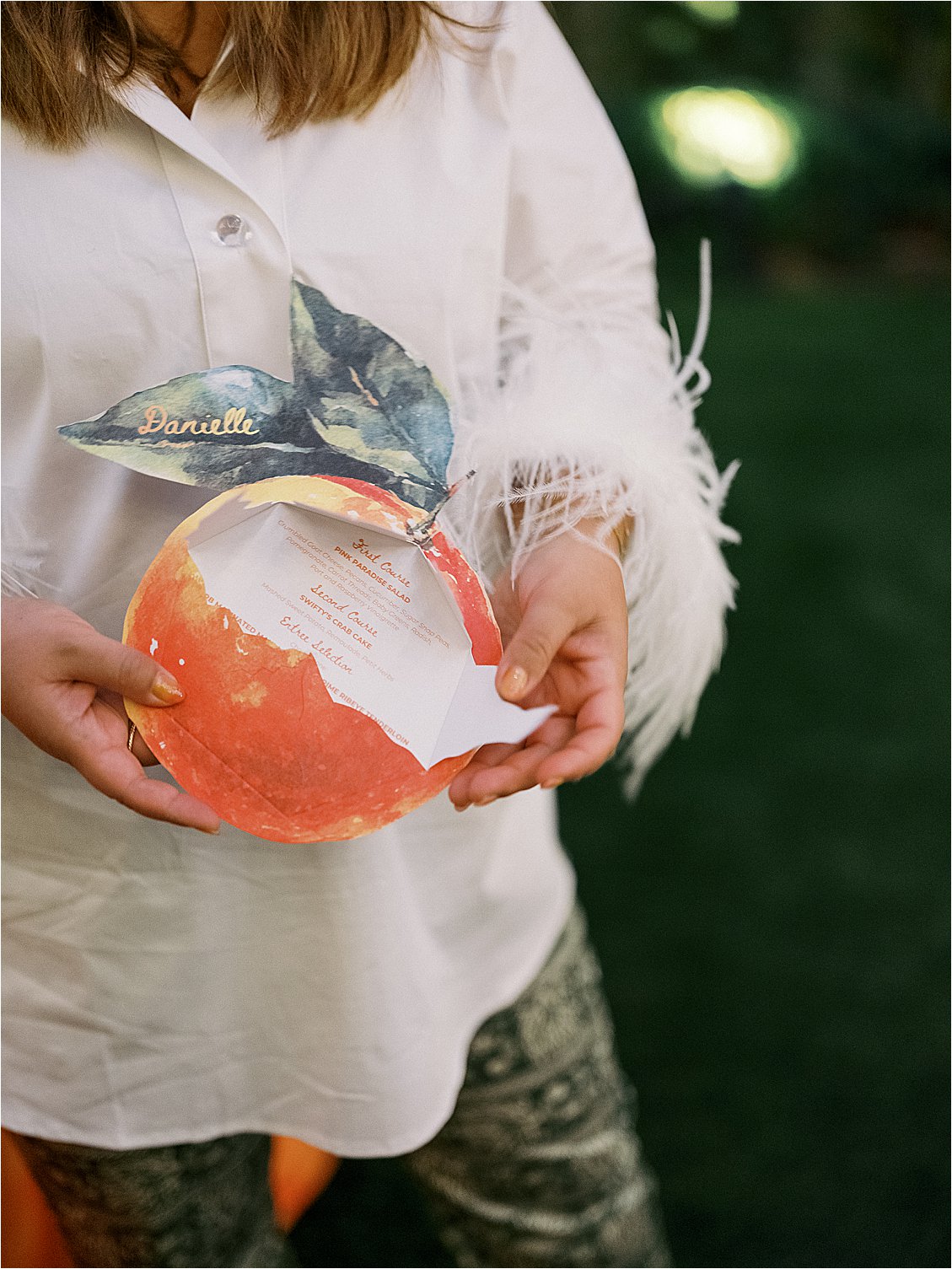 Close-up of a guest holding the personalized peelable citrus-shaped dinner menu with the name "Danielle" in gold script at The Colony Hotel Palm Beach corporate event designed by Gramercy & Grace for Zoe Strollers 