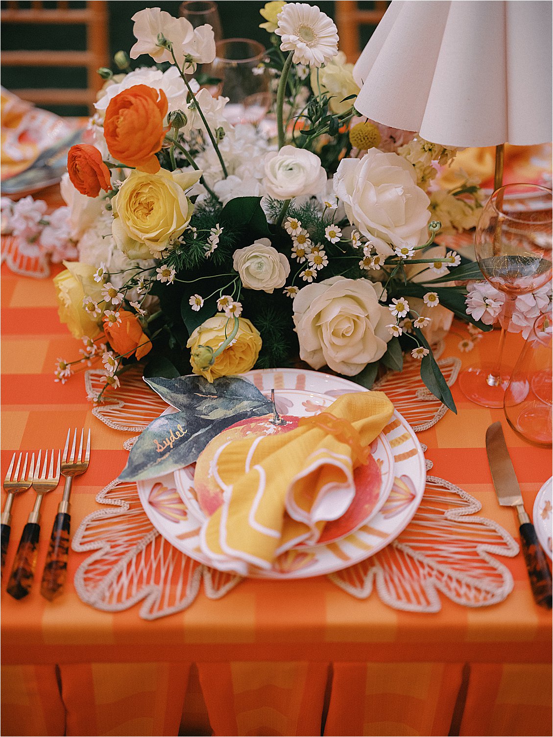 Close-up of an elegant place setting featuring a citrus-motif charger plate, golden yellow linen napkin, personalized citrus menu card, and white and yellow floral centerpiece at The Colony Hotel Palm Beach corporate dinner 