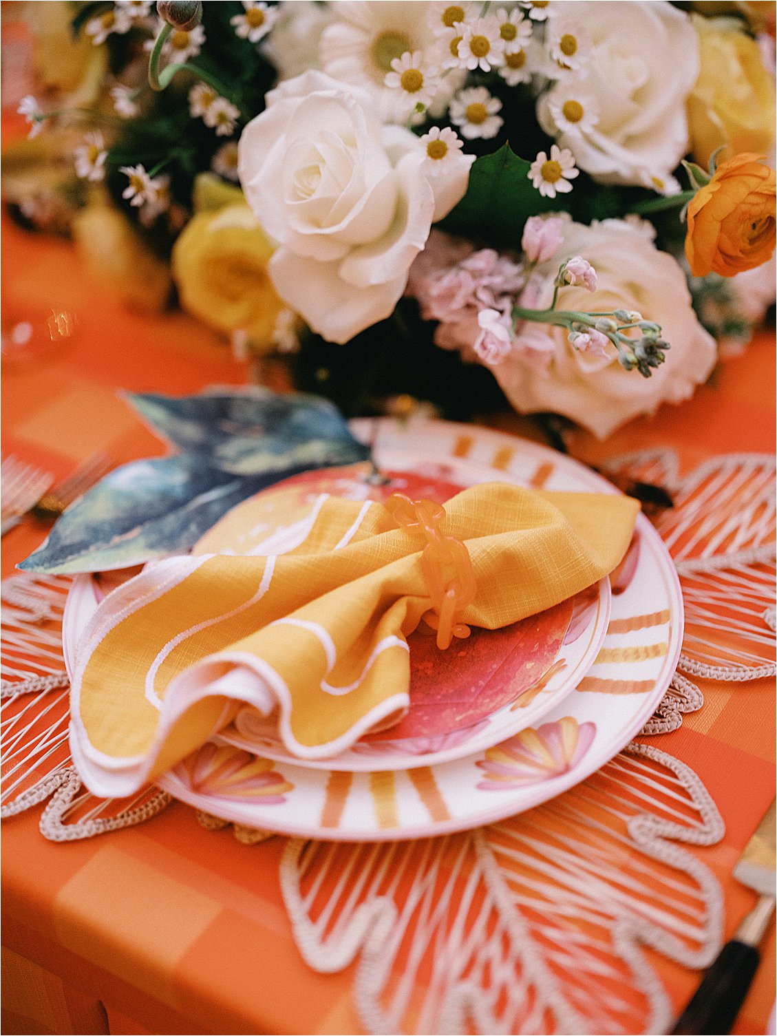 Close-up of a single citrus-motif charger plate with folded yellow linen napkin and orange acrylic napkin ring on a woven placemat, styled by Gramercy & Grace for The Colony Hotel Palm Beach corporate dinner 
