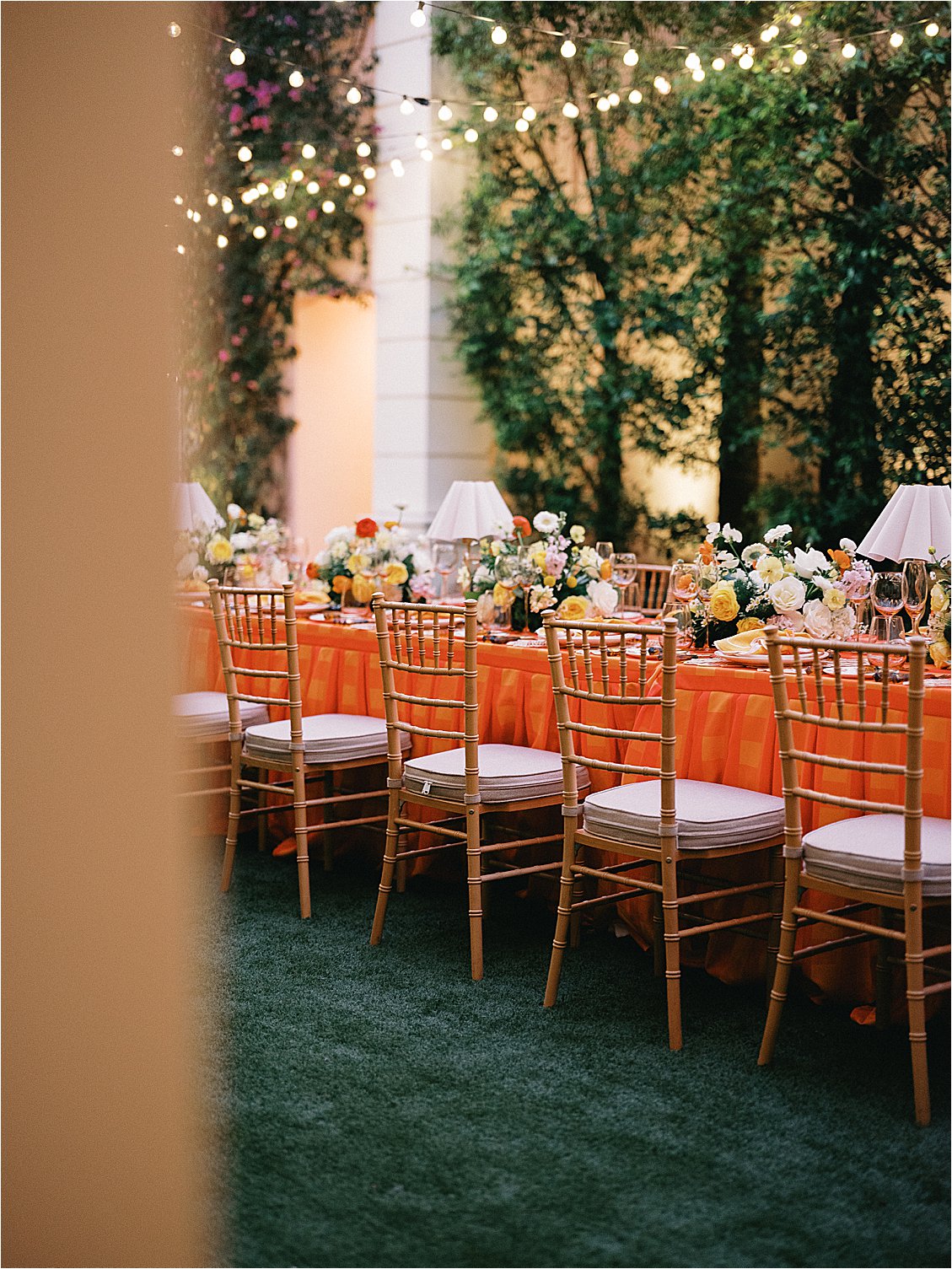 Corporate dinner table at The Colony Hotel East Garden viewed through a colonnade archway, glowing with café string lights and floral centerpieces at the Zoe Strollers corporate retreat, film photography Palm Beach 