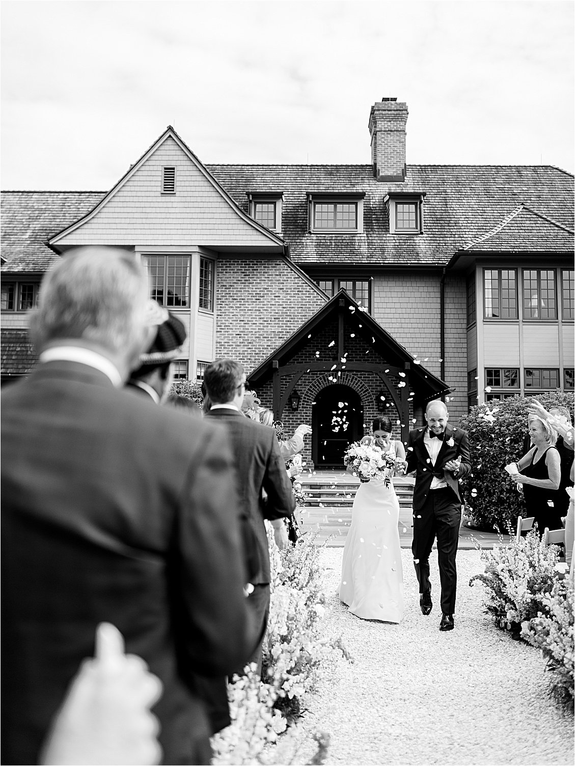 Bride and groom walking down the aisle during their ceremony recessional as guests toss flower petals at a Chesapeake Bay private estate wedding.