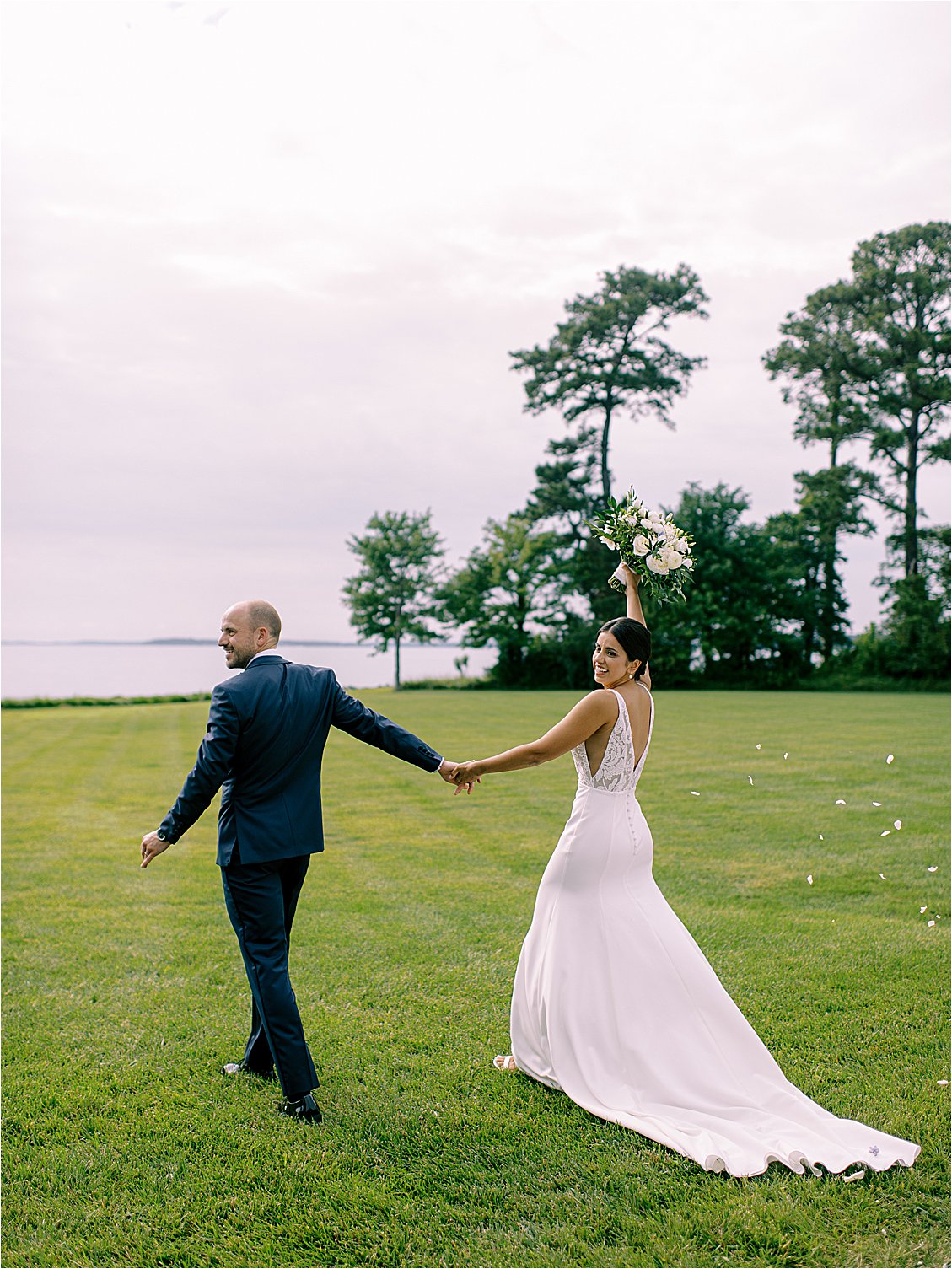 Bride and groom walking across waterfront lawn after ceremony at elegant Oxford Maryland estate wedding
