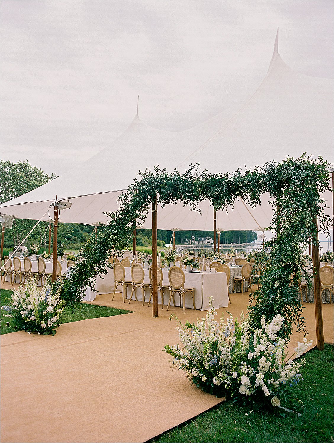 Elegant sailcloth reception tent with greenery arch overlooking waterfront at Oxford Maryland estate wedding