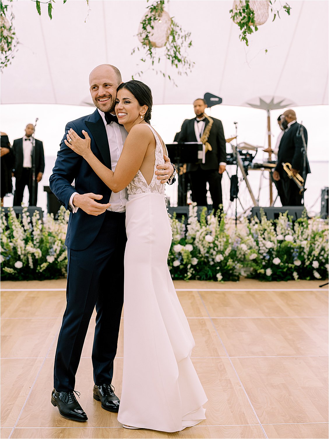 Bride and groom embracing during first dance with live band at waterfront estate wedding reception