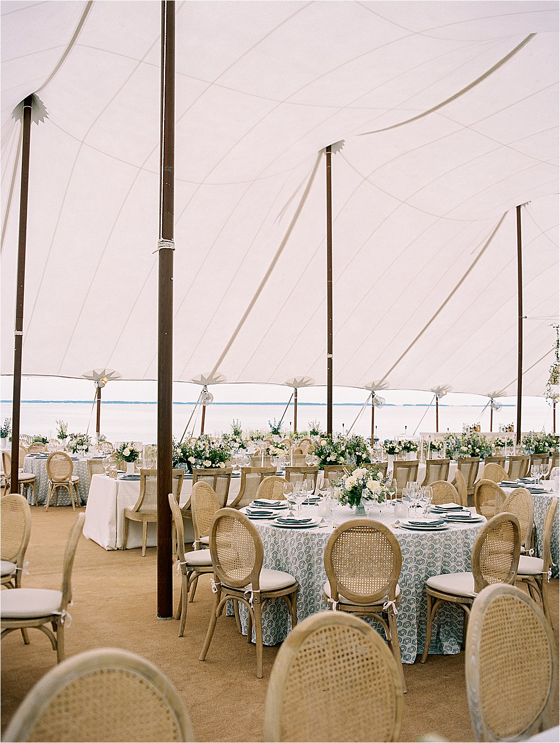 Elegant sailcloth wedding reception tent with floral tablescapes overlooking the Chesapeake Bay at a private estate wedding in Oxford Maryland.