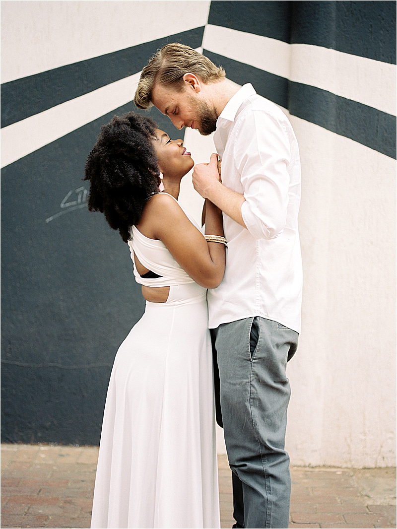 Intimate film portrait of Aisha and Kev leaning foreheads together in front of a black and white geometric mural at Maboneng Precinct, Johannesburg, South Africa, during their anniversary session photographed by Renee Hollingshead