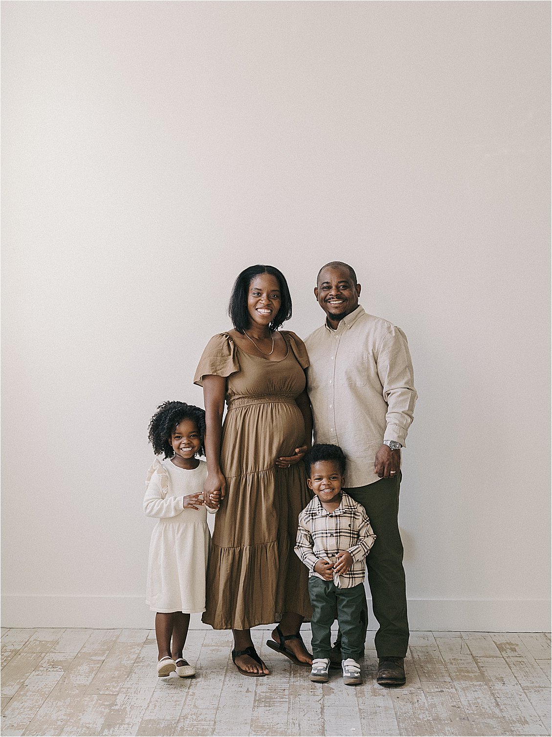 Full family studio portrait with expecting mother, father, and two young children on light wood floors, film maternity session in Annapolis Maryland by Renee Hollingshead Photography
