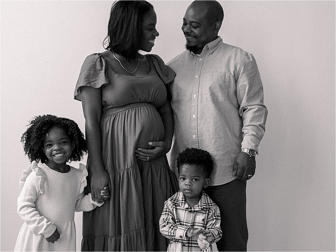 Black and white studio family portrait with expecting mother and father gazing at each other, two children in foreground, film maternity session Annapolis Maryland by Renee Hollingshead Photography