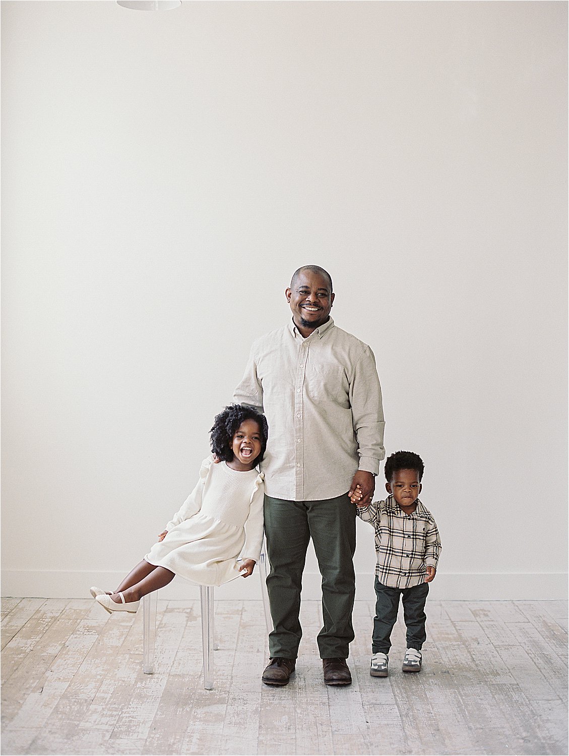 Father posing with two young children in studio, daughter perched on acrylic stool laughing, son holding dad's hand, film family portrait Annapolis Maryland by Renee Hollingshead Photography