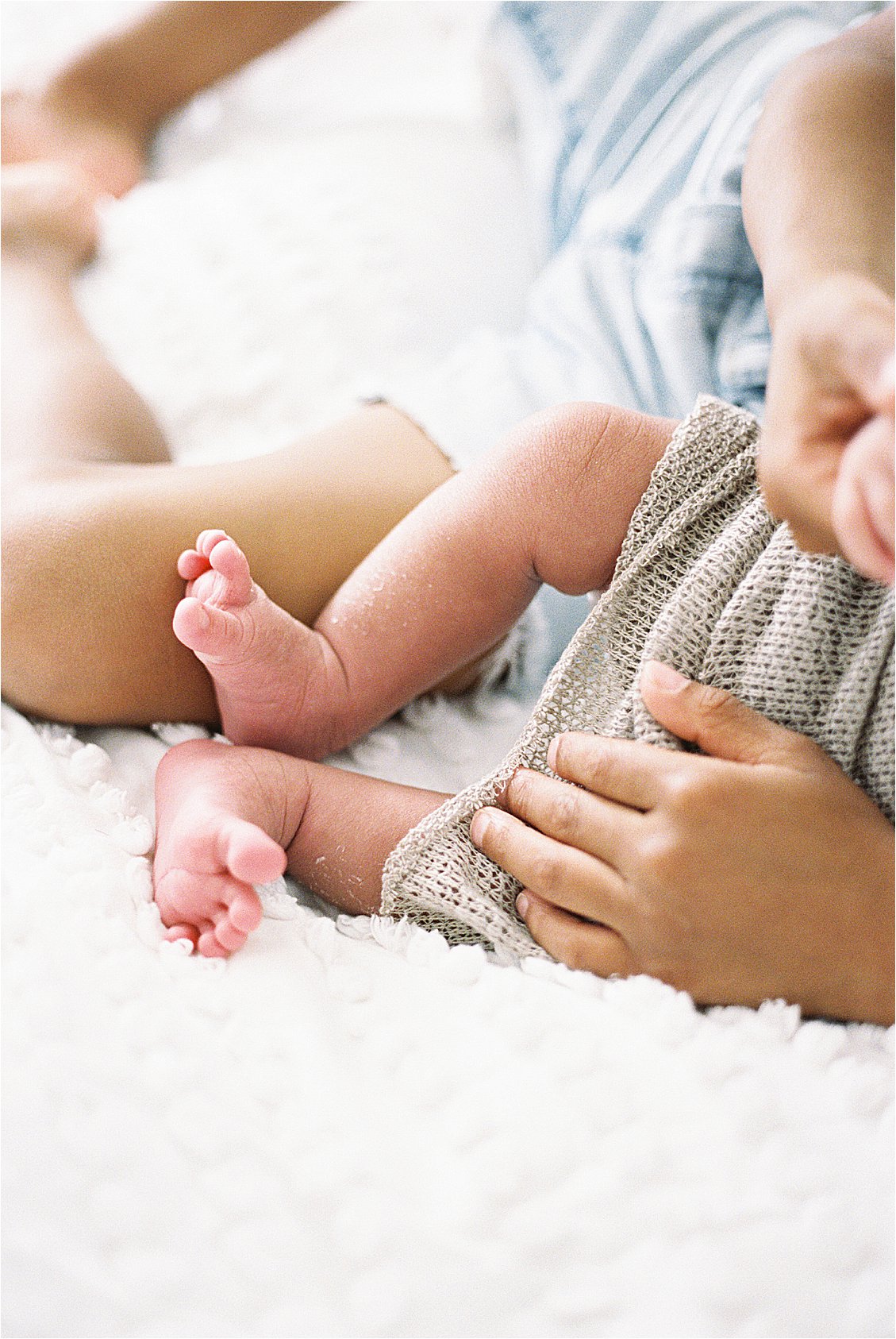 Close up of newborn baby feet and tiny hands on a white blanket, film photography by Renee Hollingshead Photography