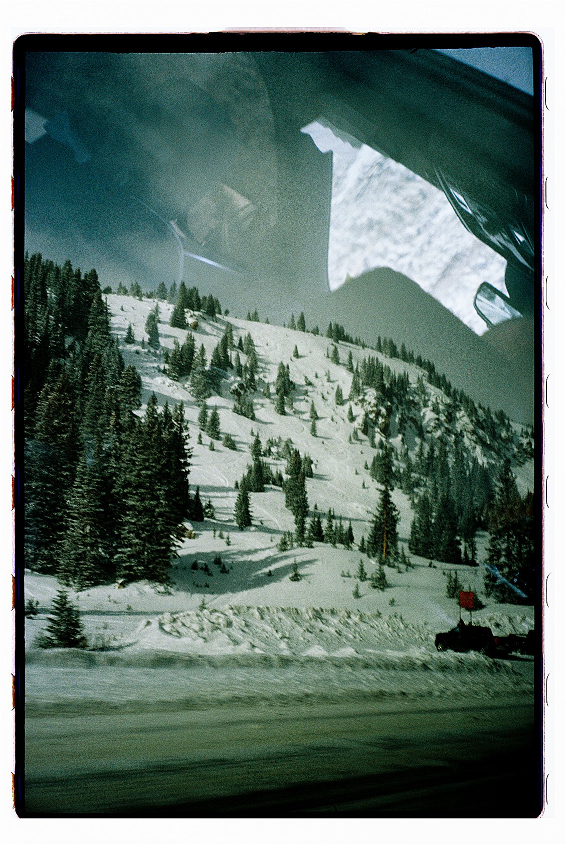 Rocky Mountain ski slope covered in snow with pine trees viewed through a car window on the road to Winter Park Colorado. Film photo by destination photographer Renee Hollingshead on Kodak Portra 400.