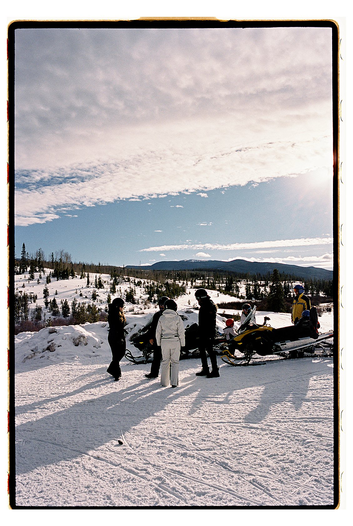 Group of snowmobilers gathered on a snowy open trail with sweeping Rocky Mountain views in Winter Park Colorado. Film photo by destination photographer Renee Hollingshead on Kodak Portra 400.