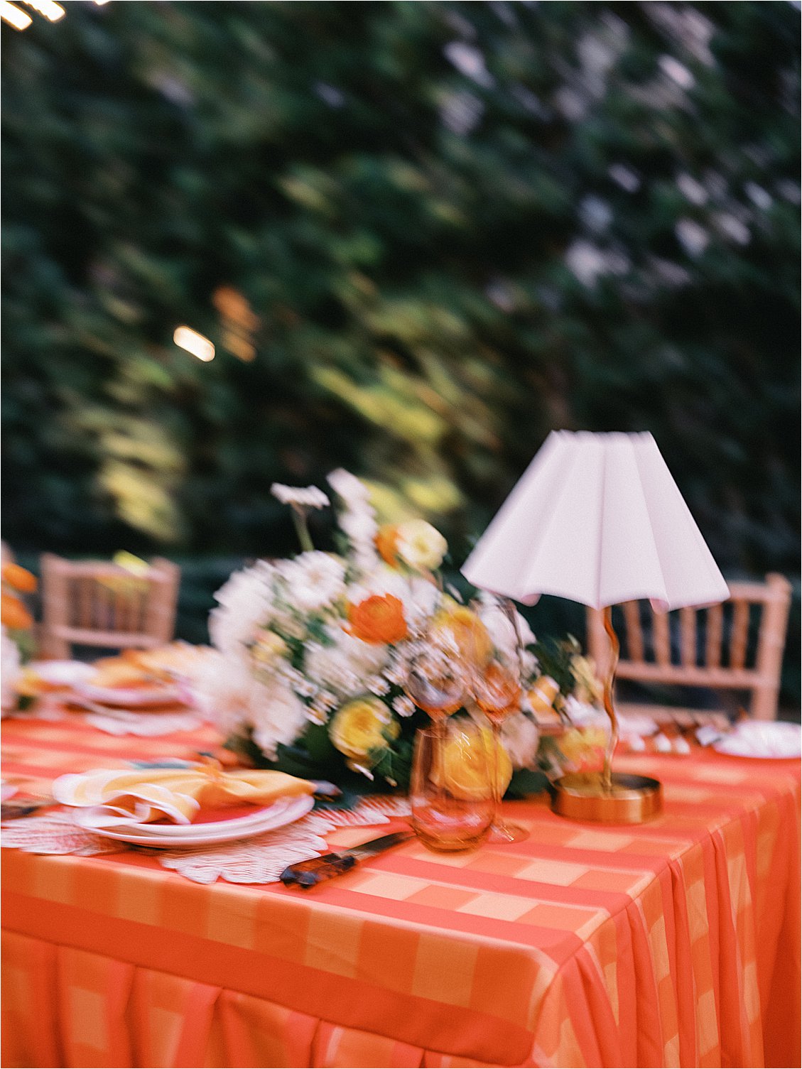 Atmospheric film photograph of the corporate dinner table with bold orange plaid tablecloth, white pleated table lamp, and citrus floral centerpiece in The Colony Hotel East Garden at twilight, Palm Beach event photography 