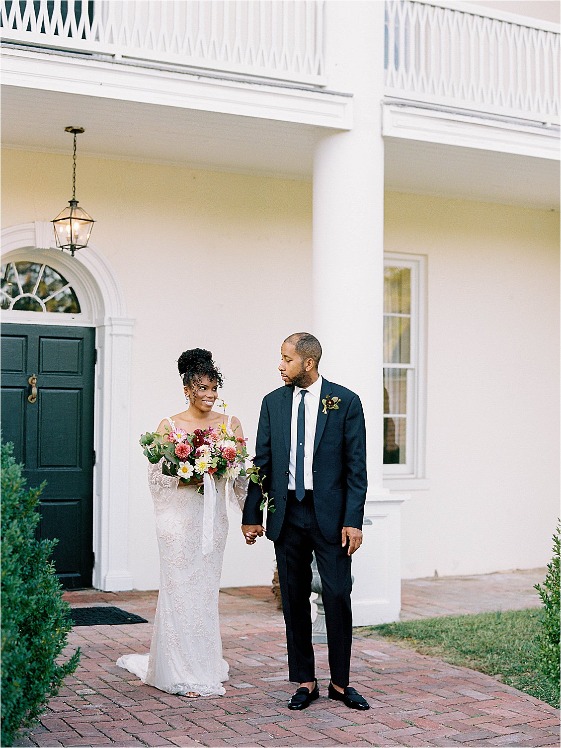 Bride and groom holding hands outside Mt. Airy Mansion in Maryland, bride smiling at groom in editorial film wedding portrait by Renee Hollingshead Photography