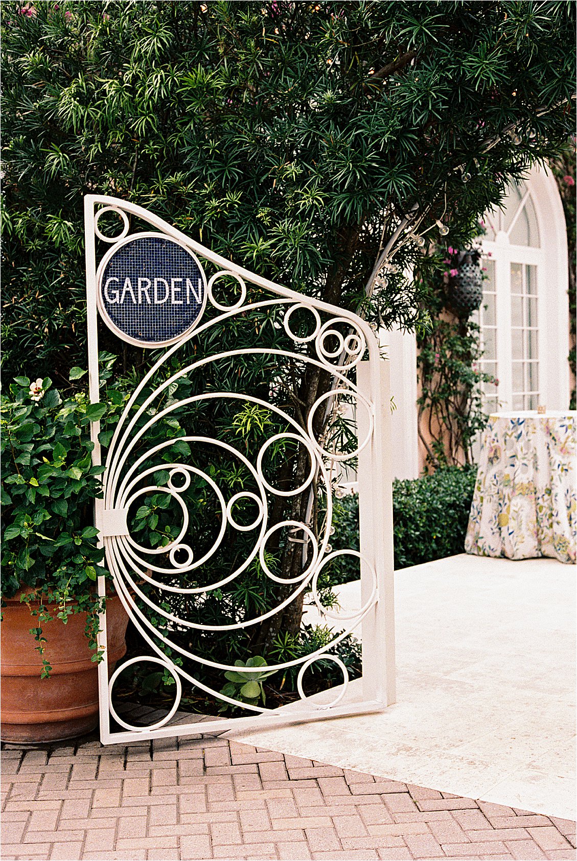 Close up of the ornate white iron Garden gate at The Colony Hotel Palm Beach with circular mosaic sign surrounded by tropical greenery, photographed on film