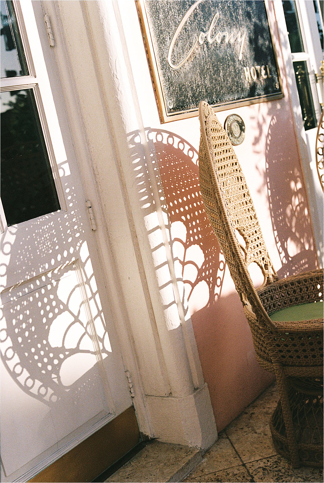 Close up film photograph of wicker peacock chair casting intricate shadow on the blush pink wall beside the Colony Hotel sign at golden hour