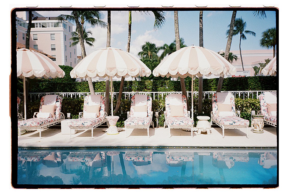 The Colony Hotel Palm Beach pool lined with white iron floral chaise lounges under fringed striped umbrellas reflecting in the still water, photographed on film