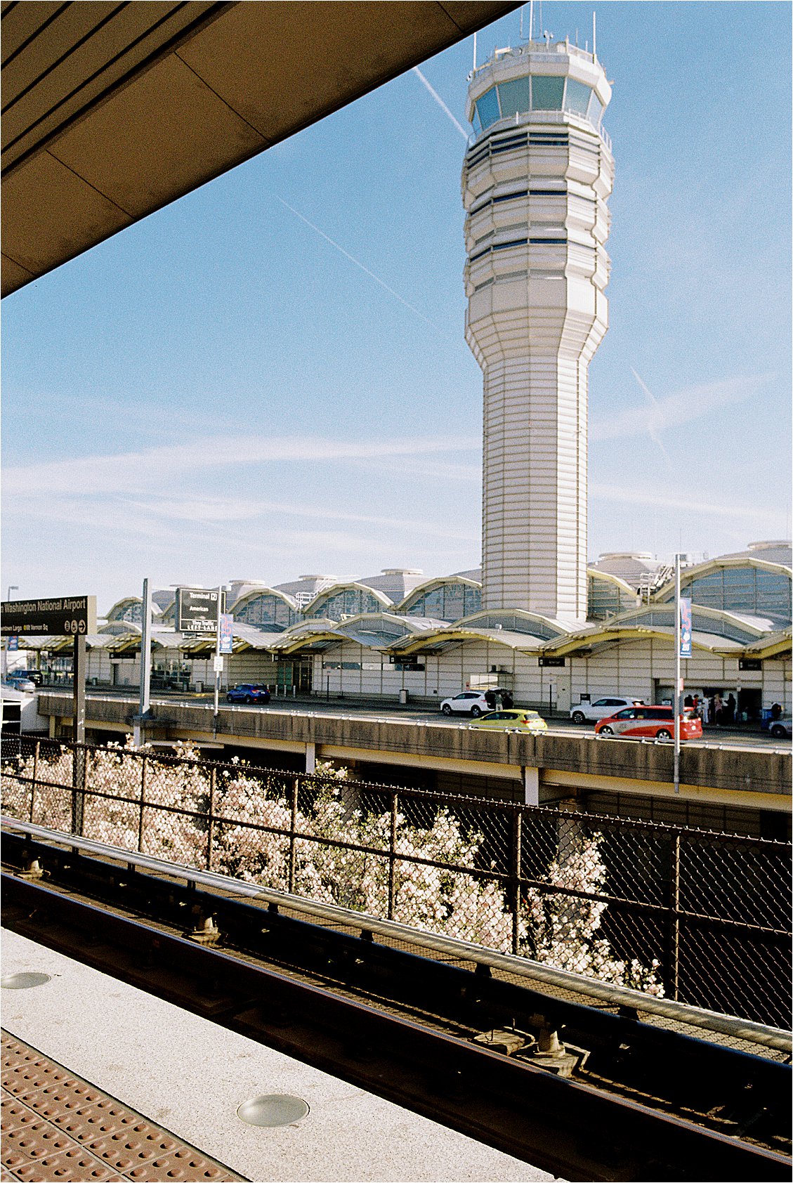 Film photograph of the air traffic control tower at Ronald Reagan Washington National Airport, with cherry blossoms blooming along the metro platform in early spring.