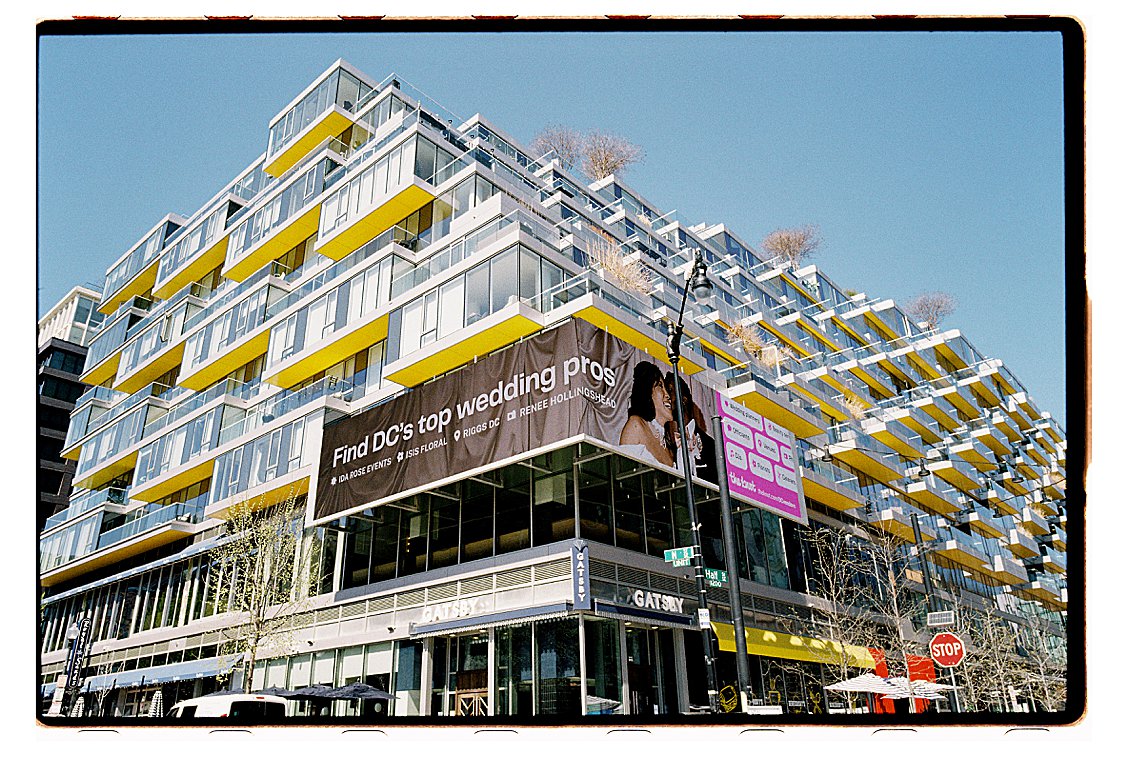 Large-format The Knot billboard on a modern building in Washington DC's Navy Yard neighborhood, reading "Find DC's top wedding pros" with Renee Hollingshead Photography featured alongside Ida Rose Events, Isis Floral, and Riggs DC.