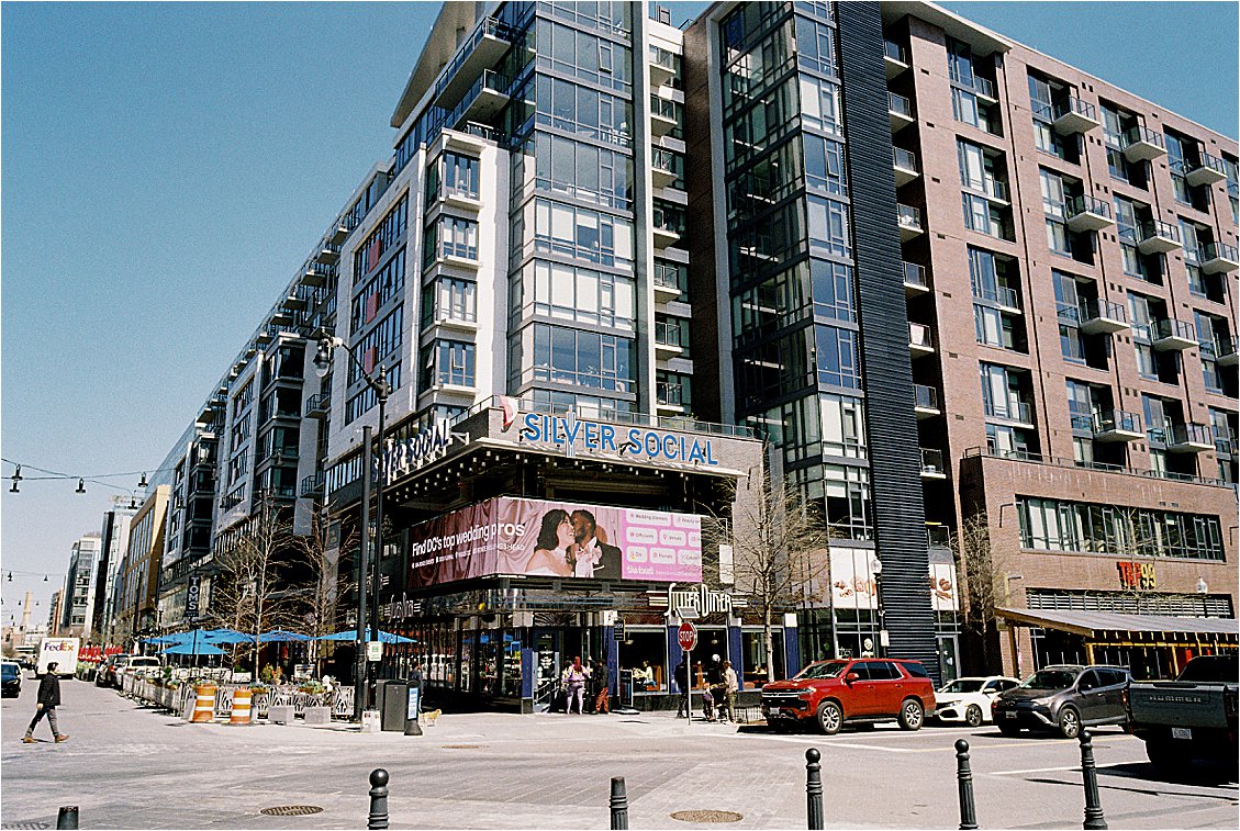 Street-level view of The Knot Washington DC billboard at Navy Yard, displayed above Silver Social on a sunny spring day, featuring Renee Hollingshead Photography as one of DC's top wedding pros.