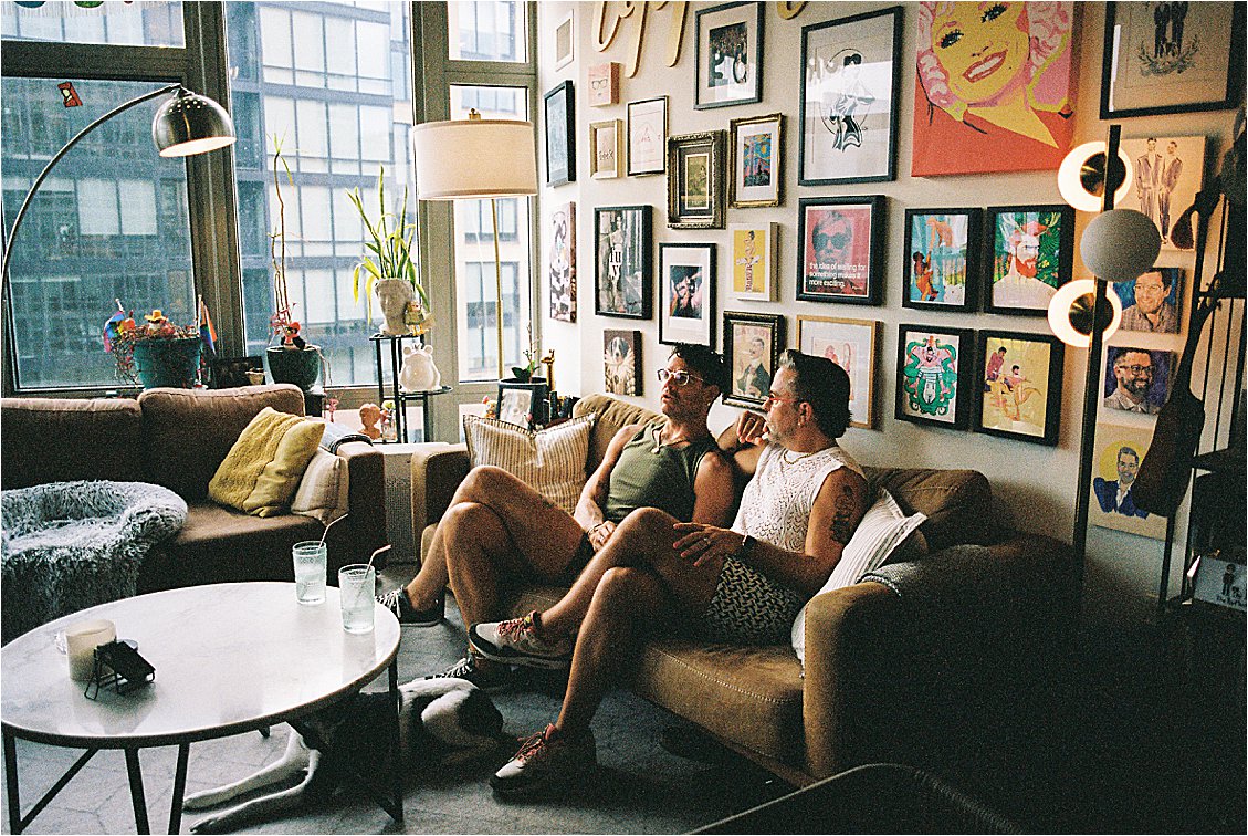 Wide film photograph of Washington DC apartment living room with floor-to-ceiling gallery wall and two men seated on couch, Kodak Portra 400, Renee Hollingshead Photography