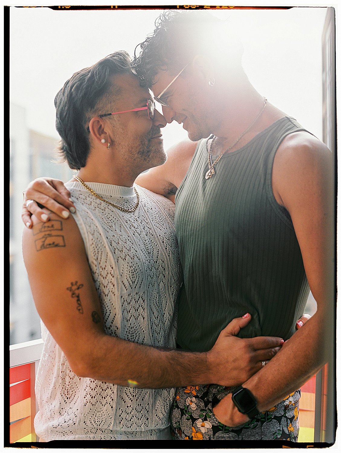 Intimate backlit portrait of two men nearly kissing on balcony with rainbow railing, Washington DC film portrait photographer Renee Hollingshead, Kodak Portra 400