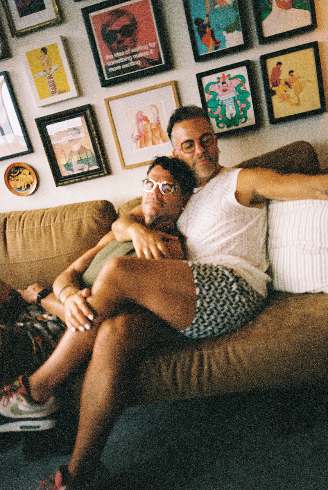 LGBTQ+ couple relaxing on couch with Andy Warhol-style prints and colorful gallery wall behind them, Washington DC anniversary film portrait session, Renee Hollingshead Photography