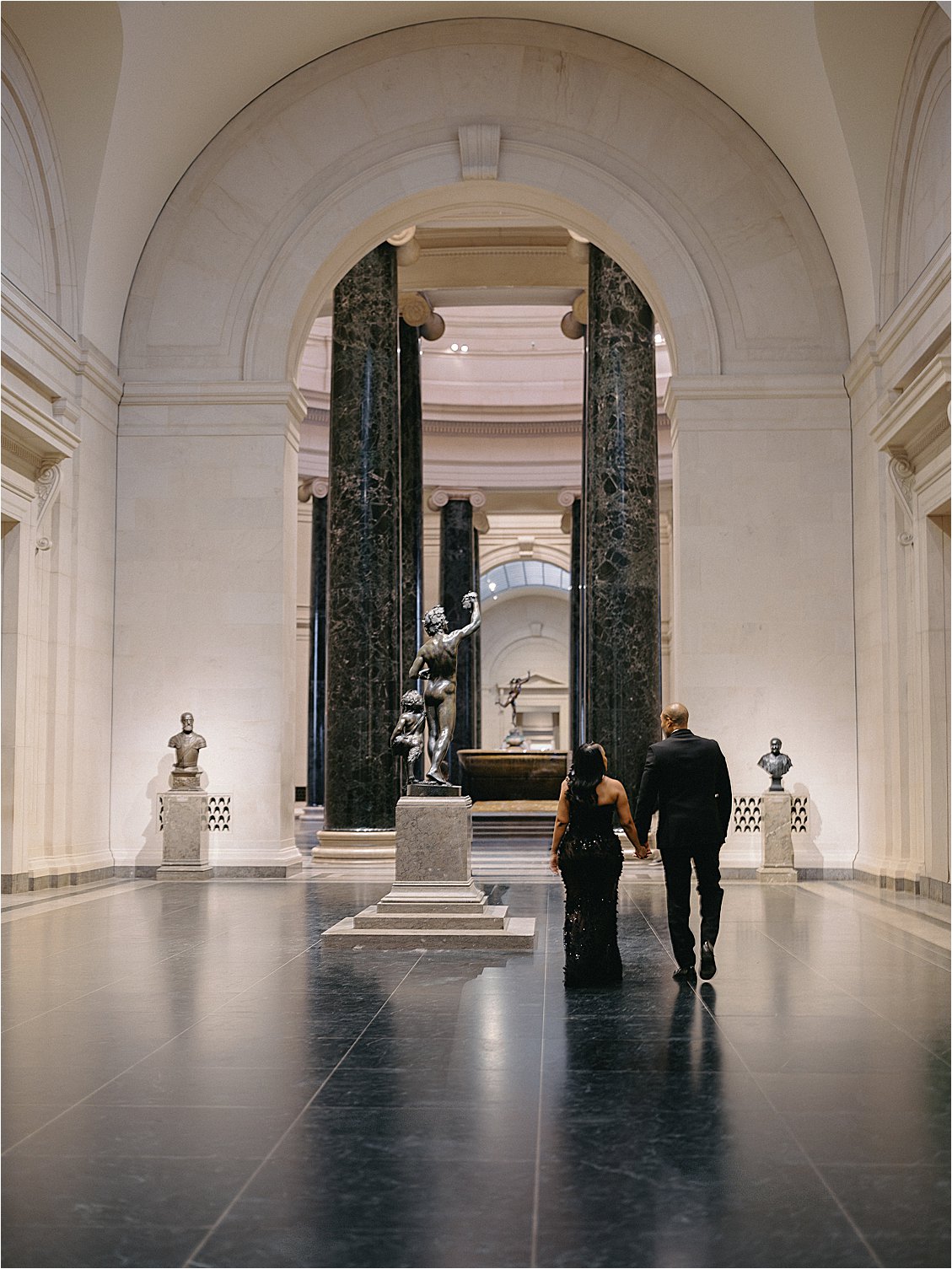 Engaged couple walking through a marble hall lined with columns during their museum engagement session in Washington, DC. Photo by destination film wedding photographer Renee Hollingshead.