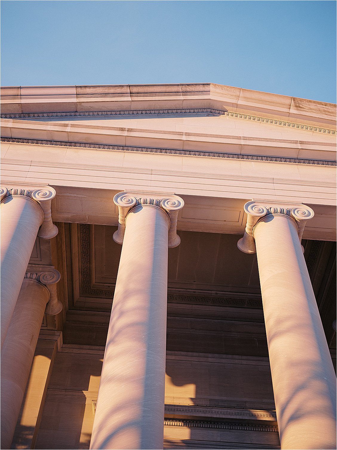 Close-up of ionic marble columns and pediment detail on a museum's exterior at golden hour. Photo by destination film wedding photographer Renee Hollingshead.